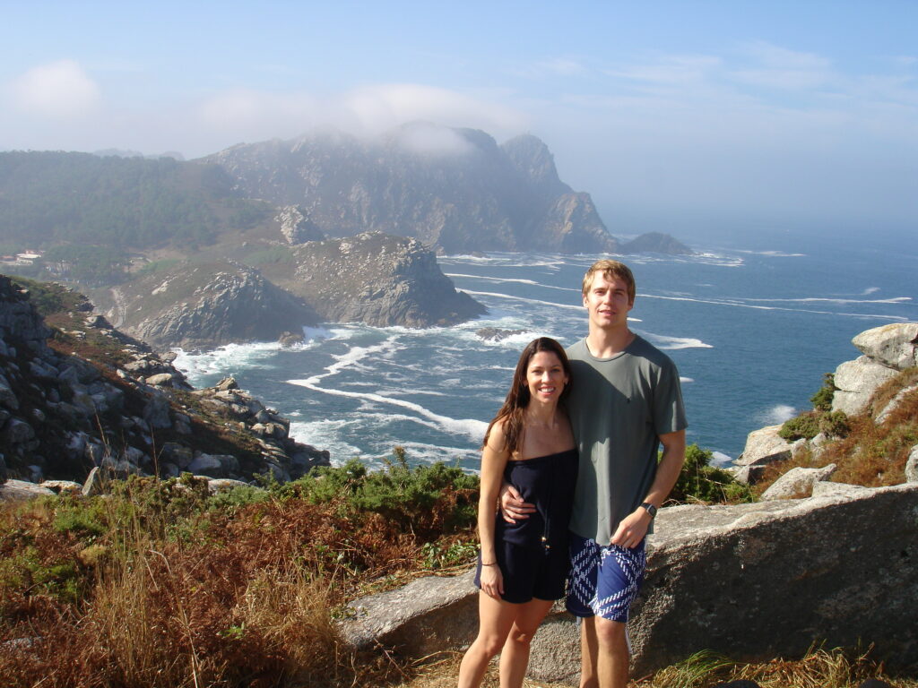 Woman in a blue top and blue shorts and man in blue shorts and a gray shirt standing in front of Islas Cies Spain