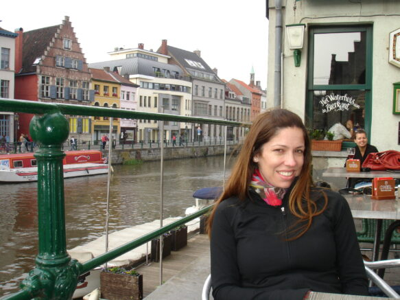 Woman in a back coat and colorful scarf in ghent belgum at a cafe in front of the canal
