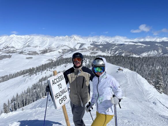 man in a tan snow suit and woman in a white coat and yellow pants next to a sign that says 