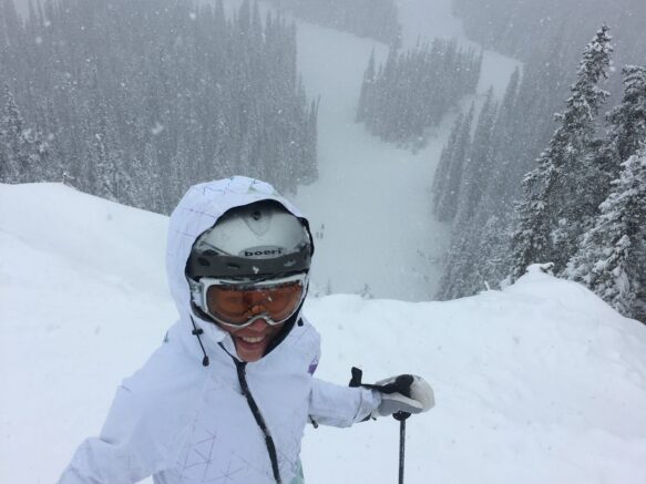 Woman in a white snow suit ready to go down a ski slope in the snow