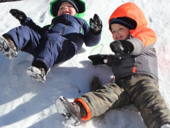 2 kids sliding down a snow hill on their backs