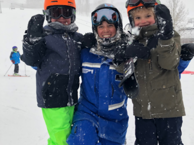 Woman in a blue snow suit between her 2 children ready to ski