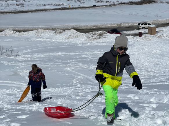 2 kids pulling sleds up the snow hill